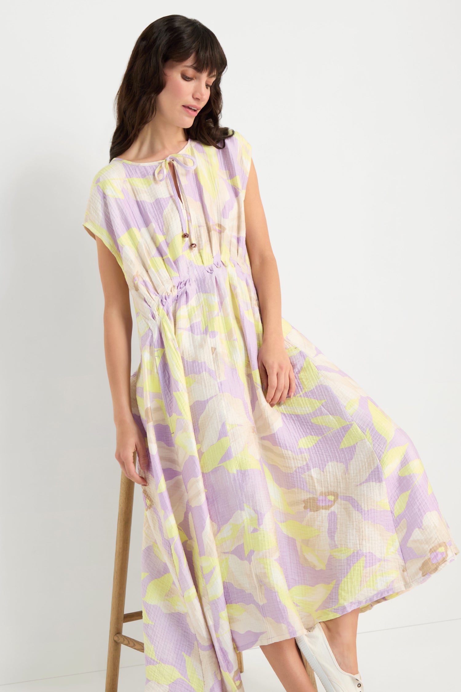 Woman wearing the Pleated Waist Print Dress, a loose-fit, pastel-printed viscose-blend dress with short sleeves and a drawstring waist, lightly holding the skirt.