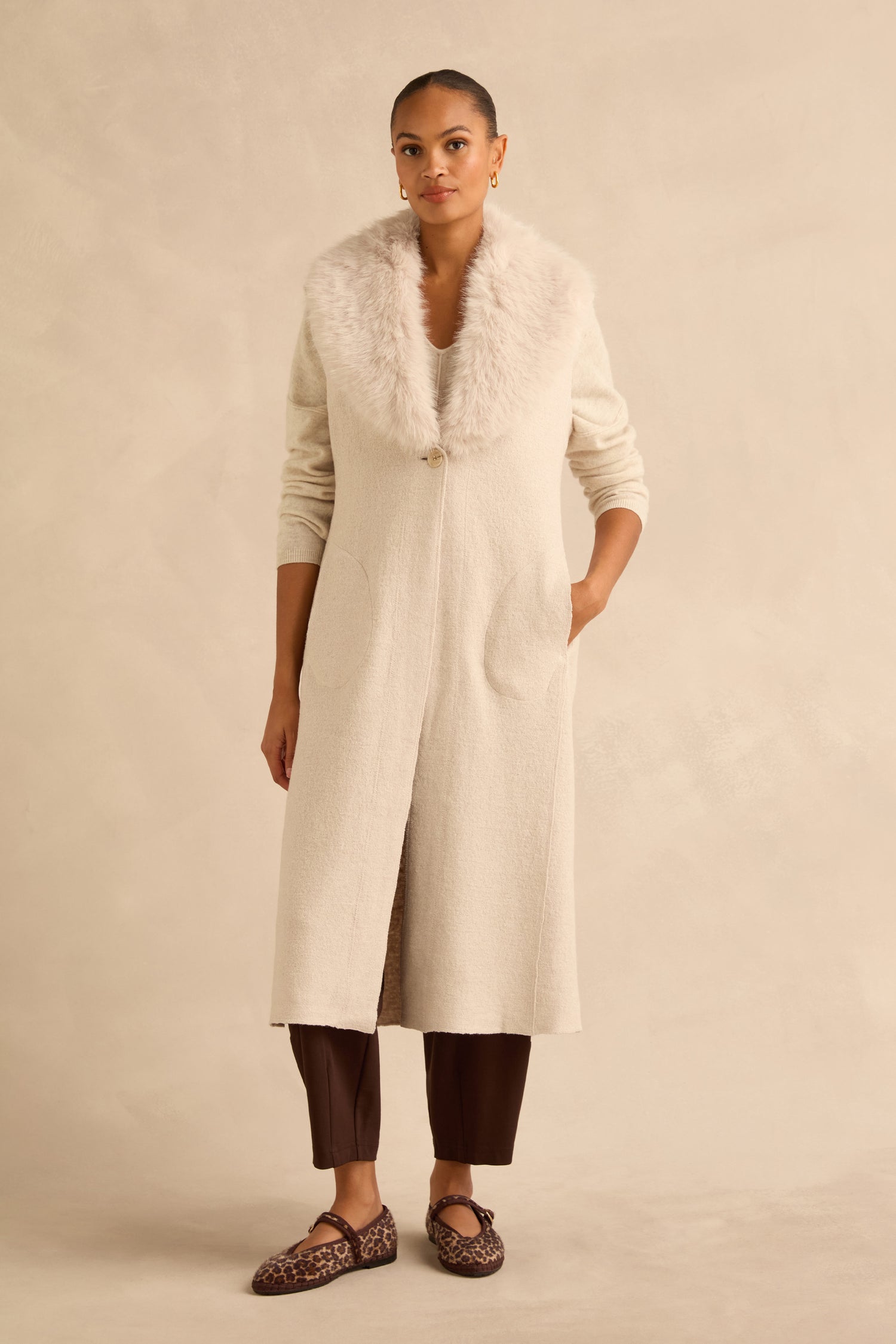 A person wears a cream-colored, single-button Detachable Fur Long Gilet over a matching sweater and dark trousers, paired with leopard-print ballet flats.
