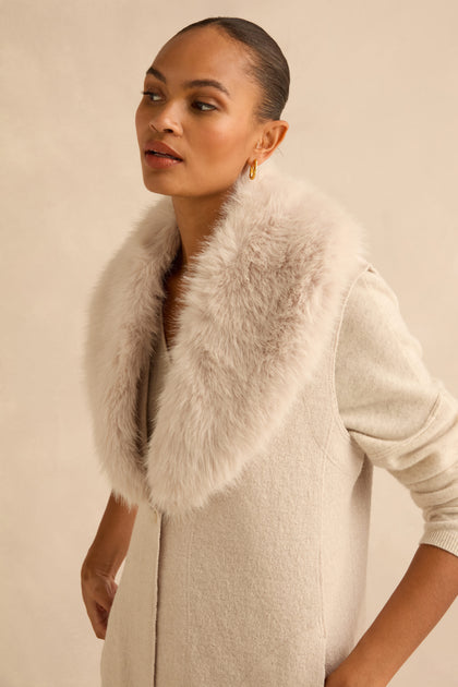 A woman wearing a Detachable Fur Long Gilet made of a wool blend with a large, detachable faux-fur collar.
