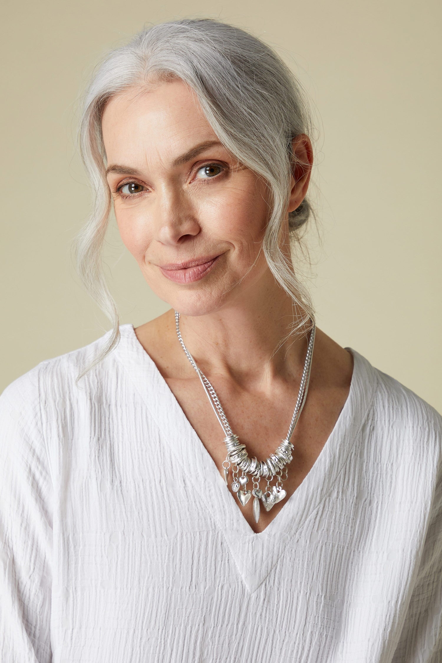 A woman with gray hair wearing a white blouse and a Silver Hearts Charm Necklace.