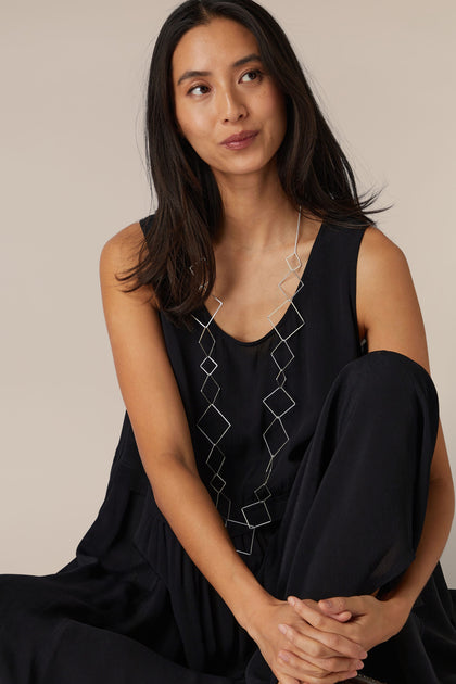 A woman in a black sleeveless top sitting with one knee up, wearing a Long Silver Squares Necklace.