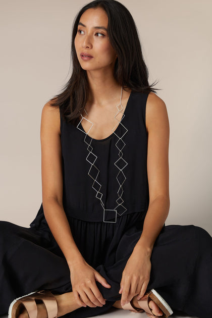 A woman in a sleeveless black outfit accessorized with the Long Silver Squares Necklace, looking to the side.