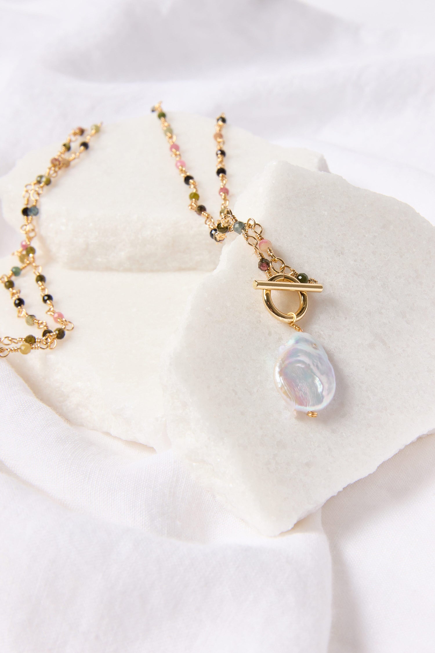 An elegant touch of a Freshwater Pearl Pendant necklace displayed on a white textured surface.