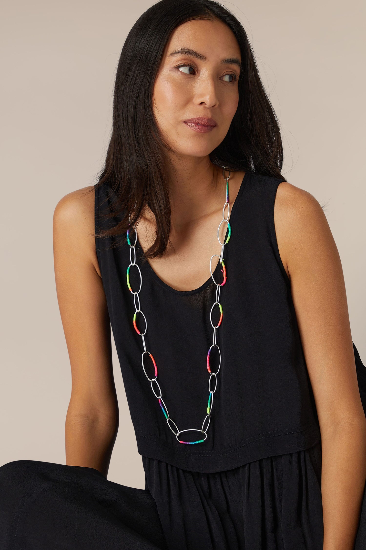 A woman in a sleeveless black top adorned with a Rainbow Stitch Silver Hoops Necklace accessory.