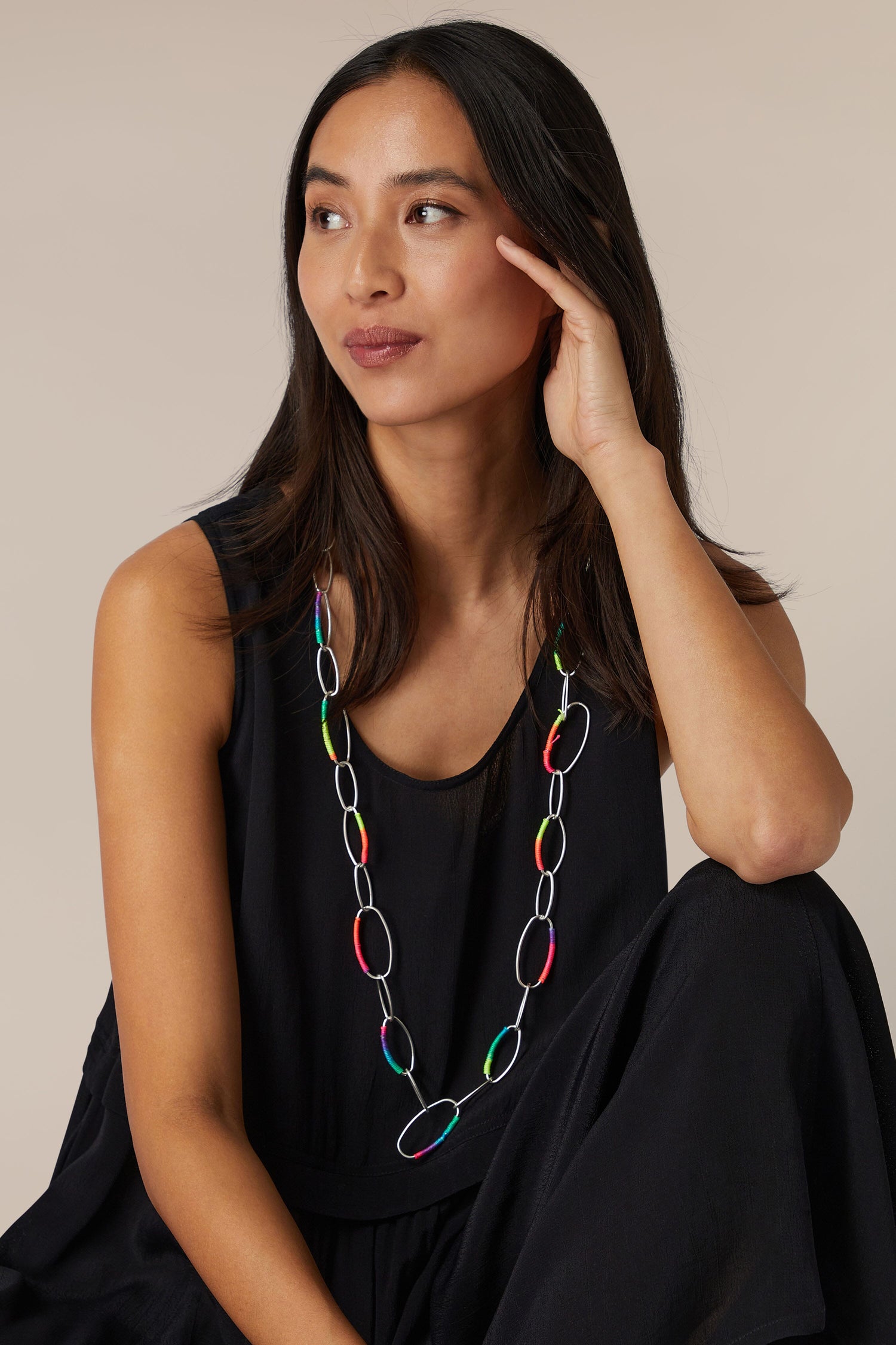 Woman in black attire with a Rainbow Stitch Silver Hoops Necklace looking thoughtfully to the side.