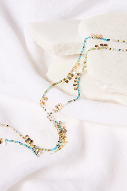 Long Turquoise Bead Necklace laid out on a white fabric surface.