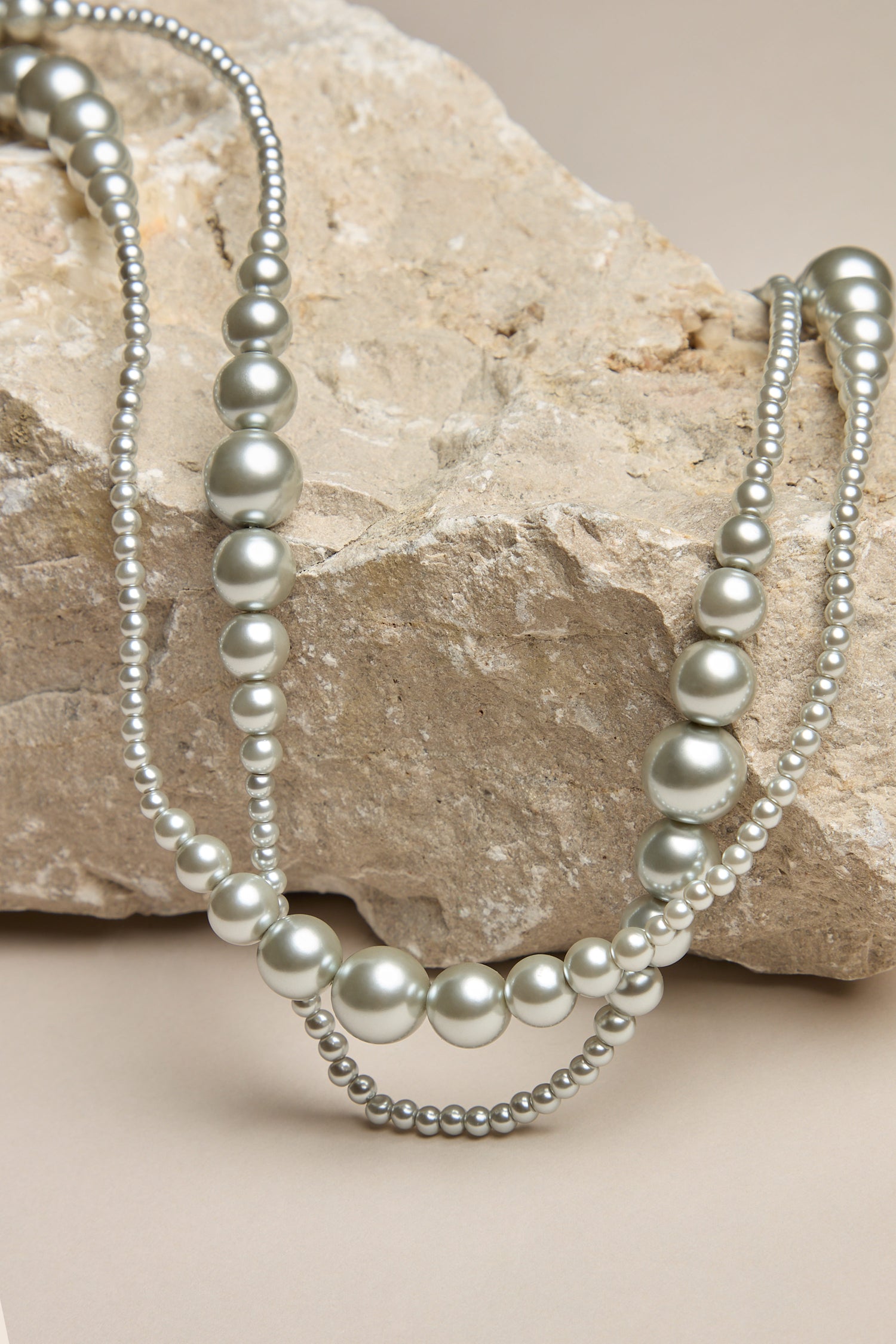 The Graduated Pearl Necklace, radiating timeless elegance, drapes over a rough beige rock placed against a neutral background.