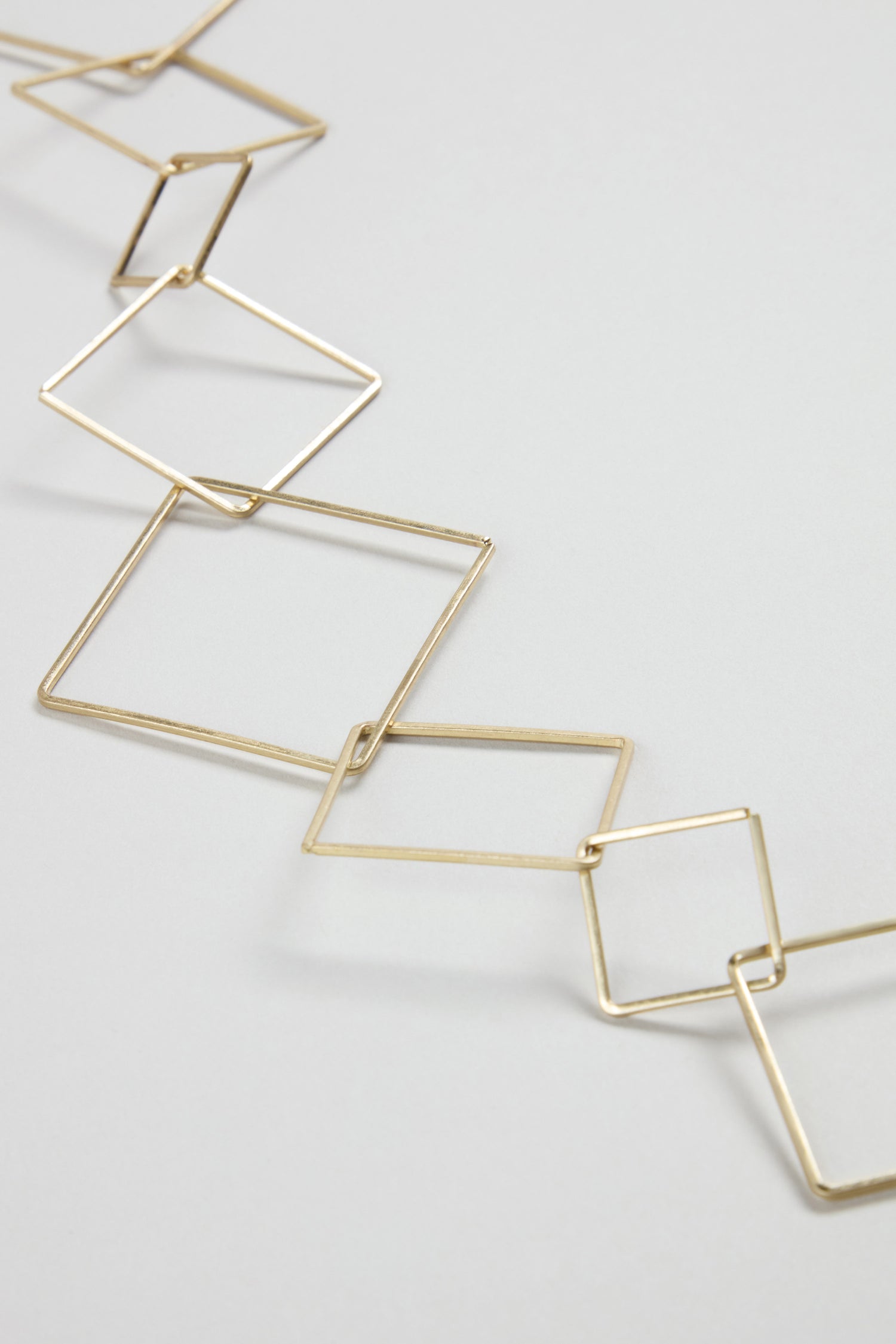 The Gold Long Squares Necklace features interconnected open square shapes arranged diagonally, offering a modern geometric style on a gold-toned chain to elevate any outfit.
