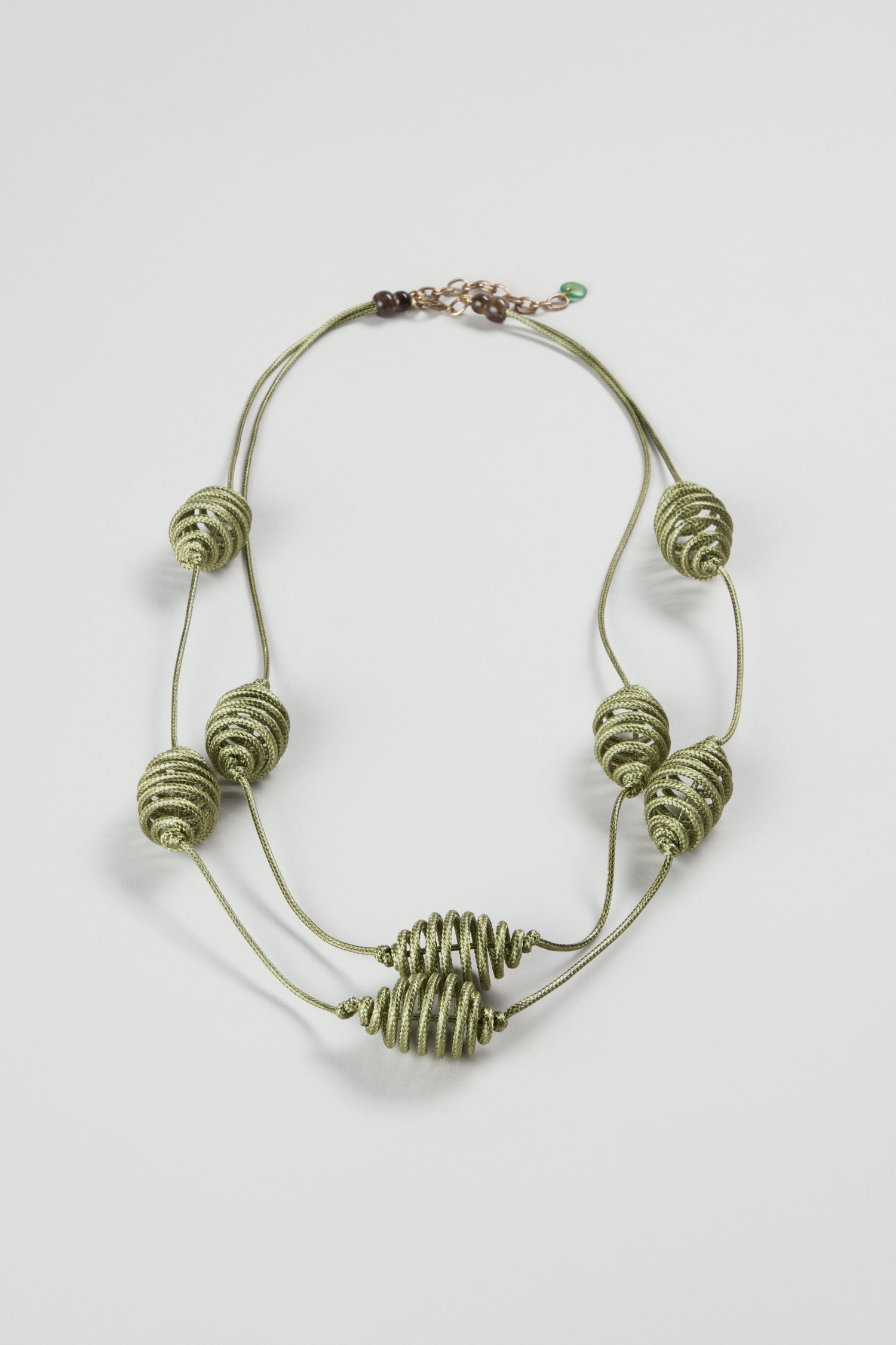The Spiral Cord Khaki Necklace features a double-strand design with green cord and eight spiral-wrapped bead accents, arranged symmetrically on a white background—a bold statement piece for any style.