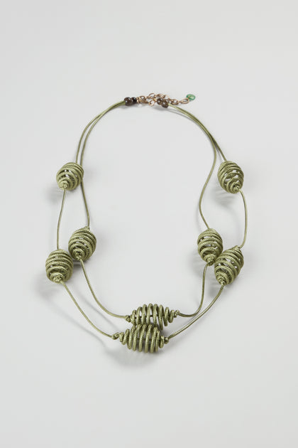The Spiral Cord Khaki Necklace features a double-strand design with green cord and eight spiral-wrapped bead accents, arranged symmetrically on a white background—a bold statement piece for any style.