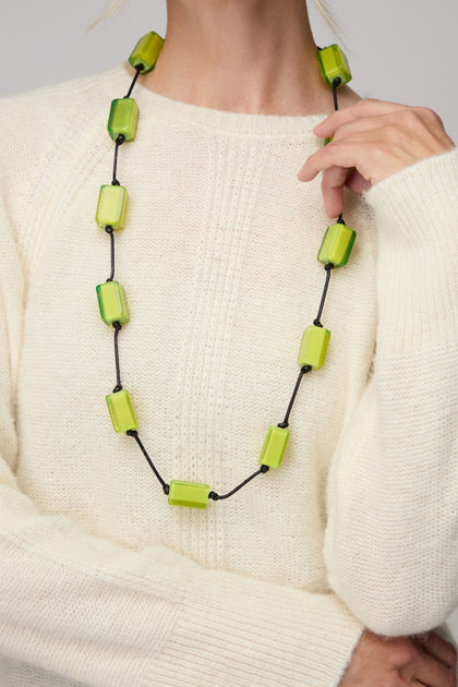 Person wearing a cream knit sweater and the Neon Resin Cubes Necklace, which features large rectangular green resin cubes on a black cord.