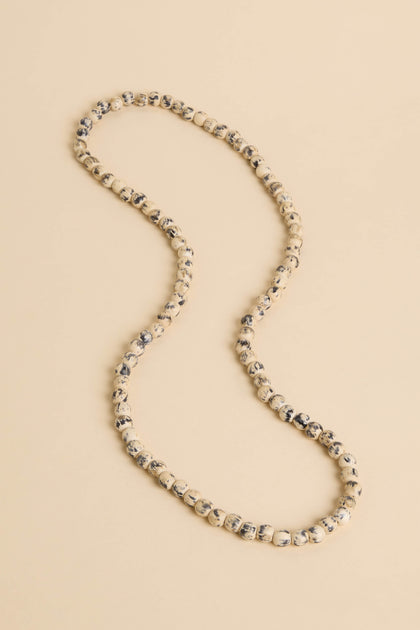 The Painted Spheres Necklace, featuring cream and black marbled round beads, is displayed on a neutral beige surface.