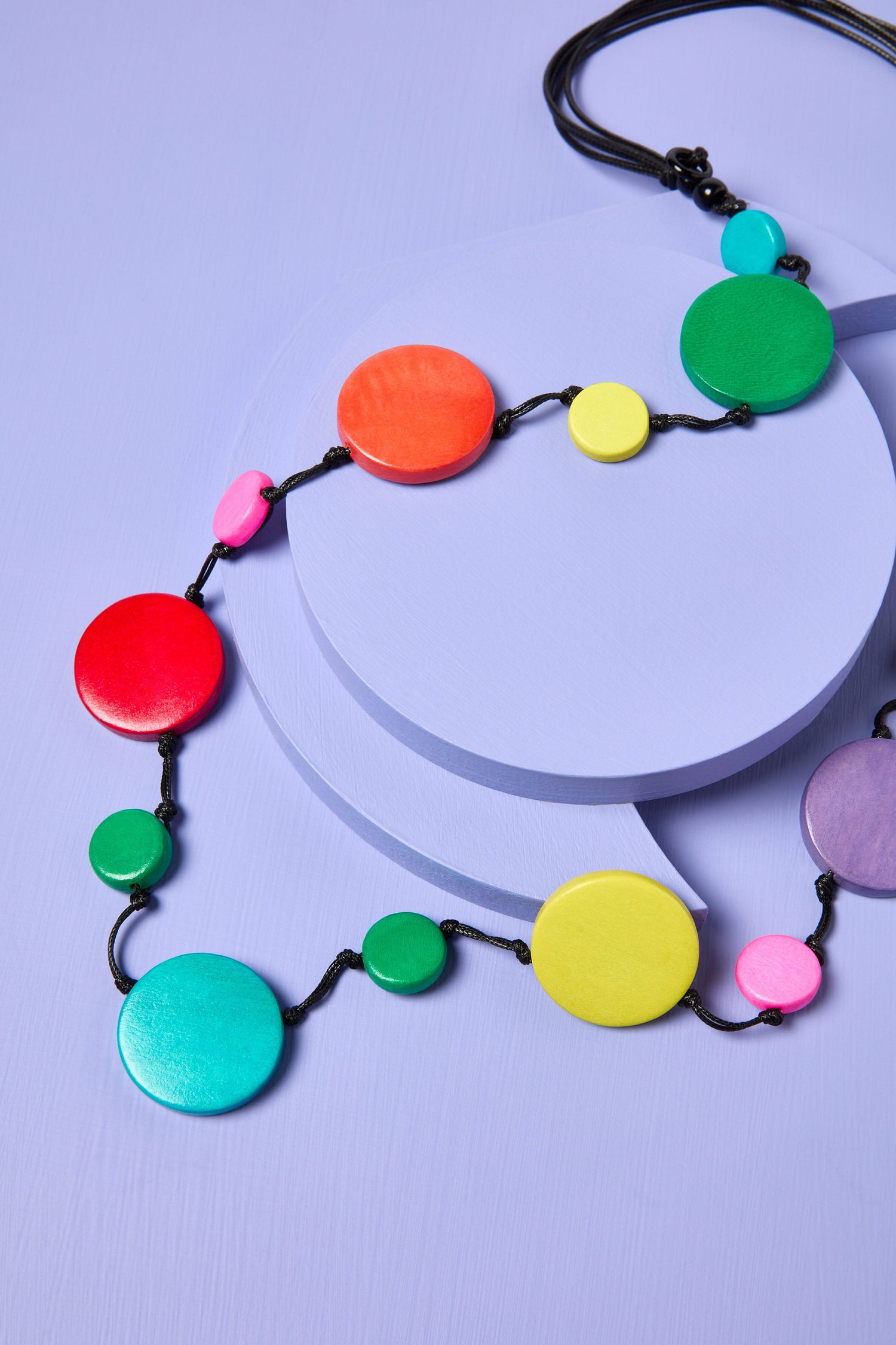 A colorful Galaxy Pendant Necklace arranged on a purple surface with a circular platform, featuring adjustable wooden discs.