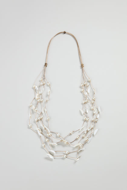 The Cascade Pearl Necklace is a versatile multi-strand piece with white beads and pearl-like leaf shapes, all linked by thin beige cords, beautifully displayed on a plain background.