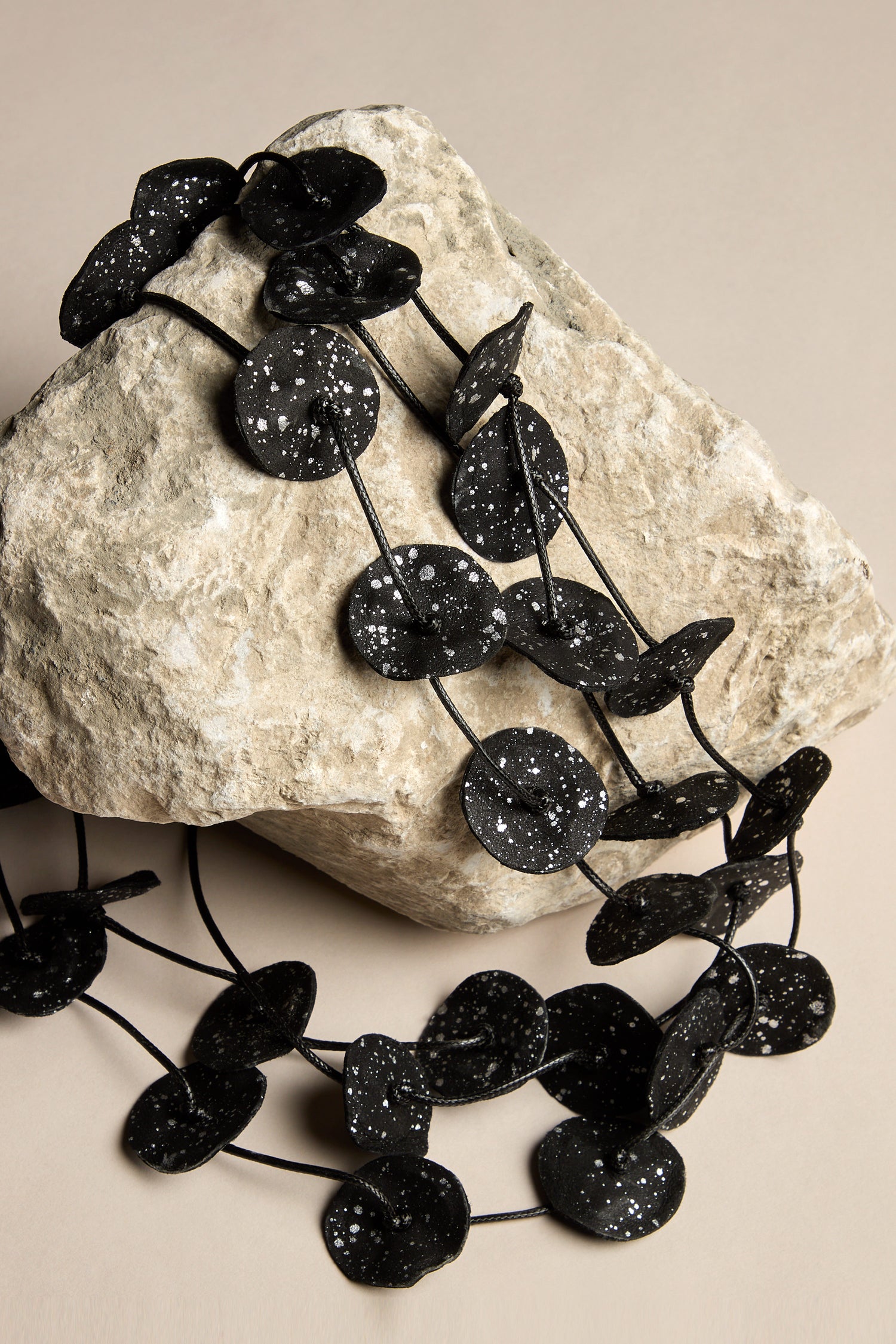 Black decorative garland with white speckles, just as versatile as the Painted Petals Necklace, elegantly draped over a large rock on a beige background.