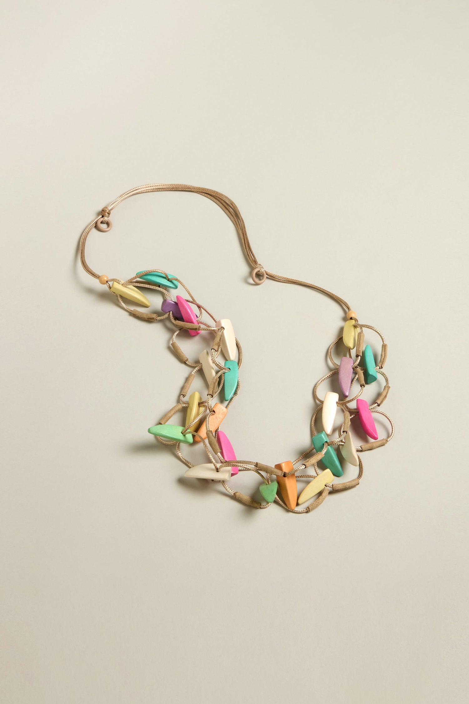 The Pastel Shapes Cord Necklace features interlinked oval beads in soft pink, green, yellow, and blue on a light beige cord—an adjustable design makes it an easy statement piece.