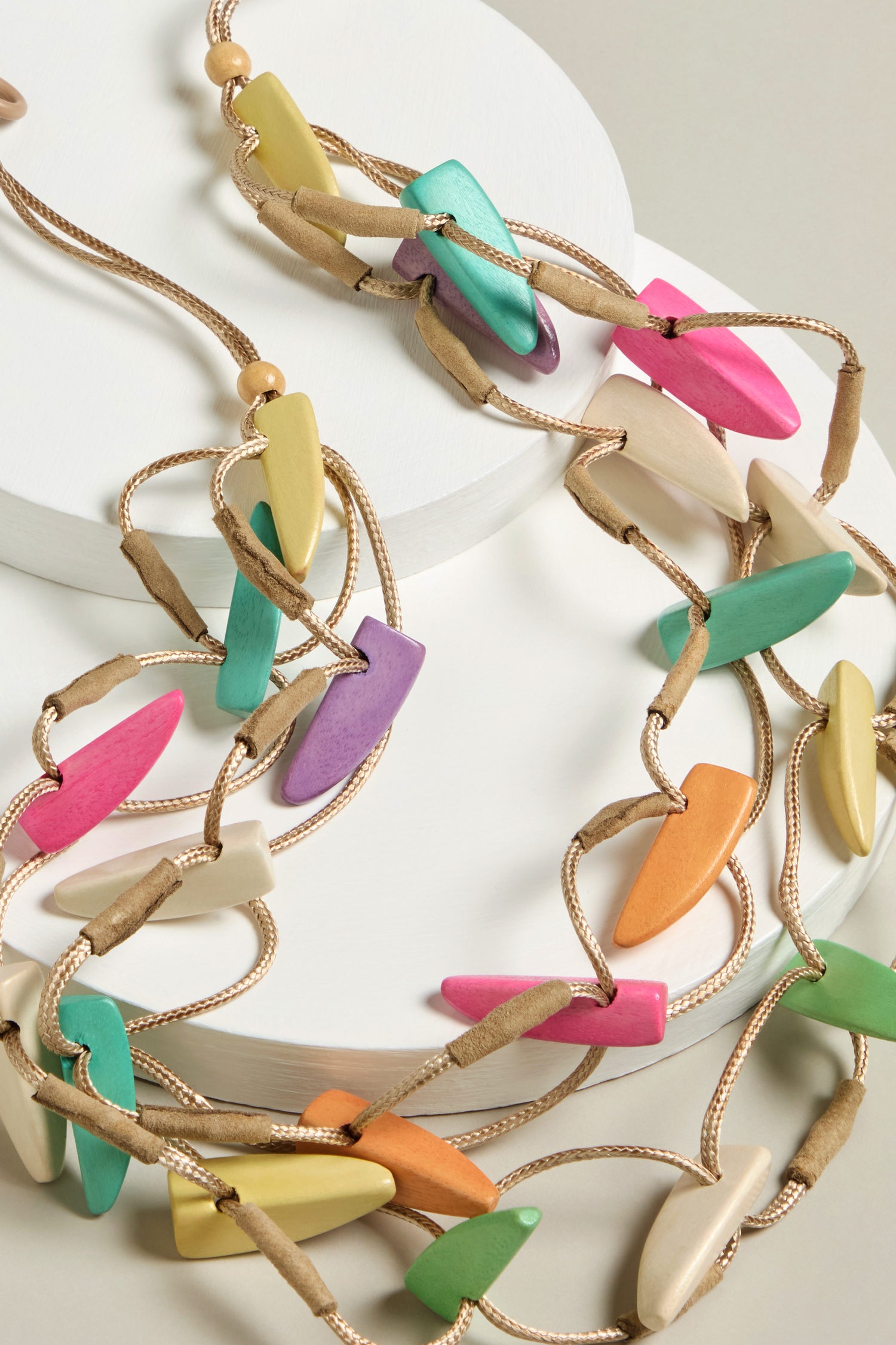 The Pastel Shapes Cord Necklace showcases multicolored, irregular beads on a tan adjustable cord—an eye-catching statement piece.