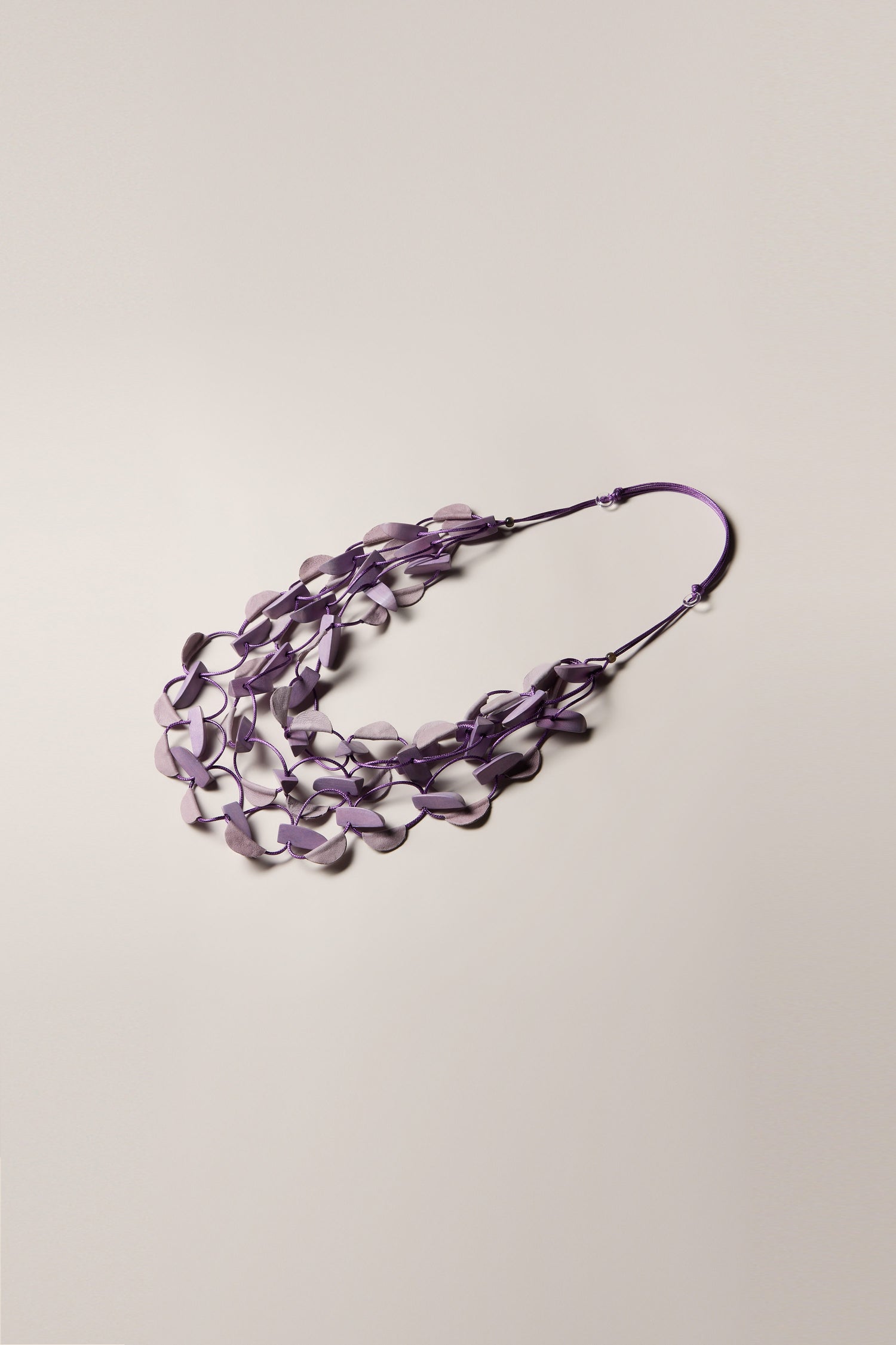 The Metallic Shapes Necklace showcases an intricate arrangement of interconnected purple wooden shapes, elegantly laid flat against a light beige background.