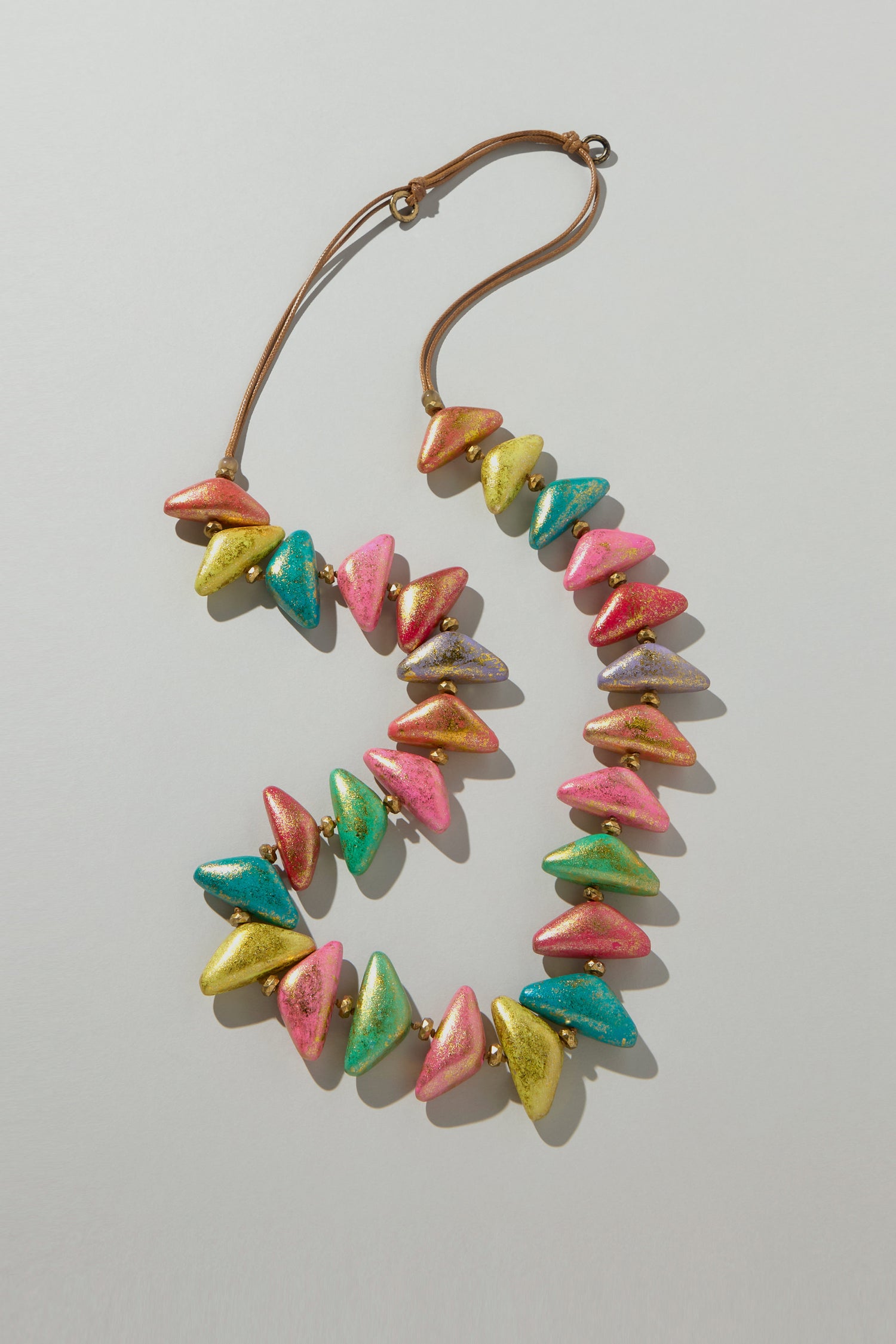 The Metallic Triangles Necklace showcases a colorful, sculptural elegance with iridescent triangular beads in pink, green, yellow, and blue hues on a neutral background.