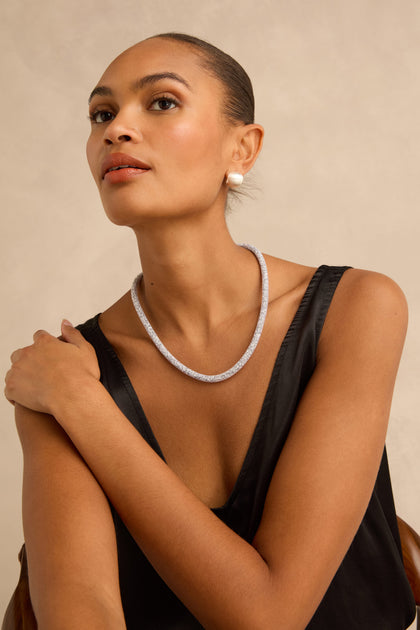 A person wearing a Short Silver Diamante Necklace and a pearl stud earring.