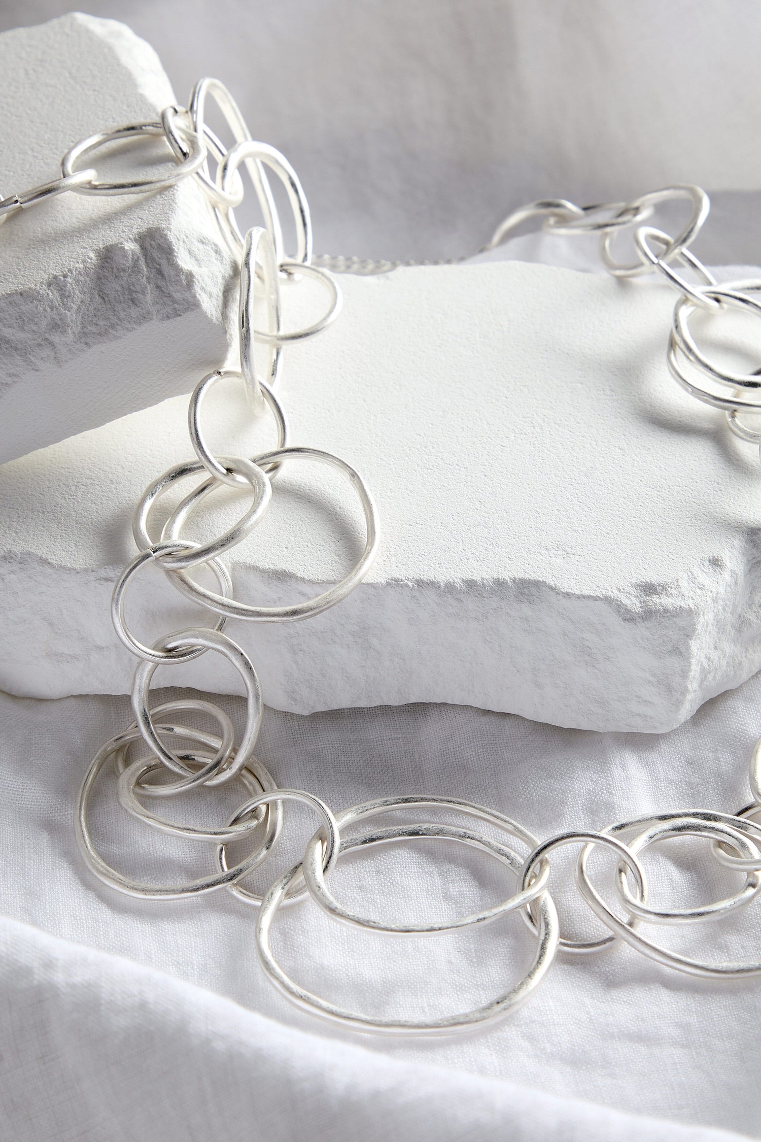 A Silver Hoops Necklace, laying on top of a white surface.