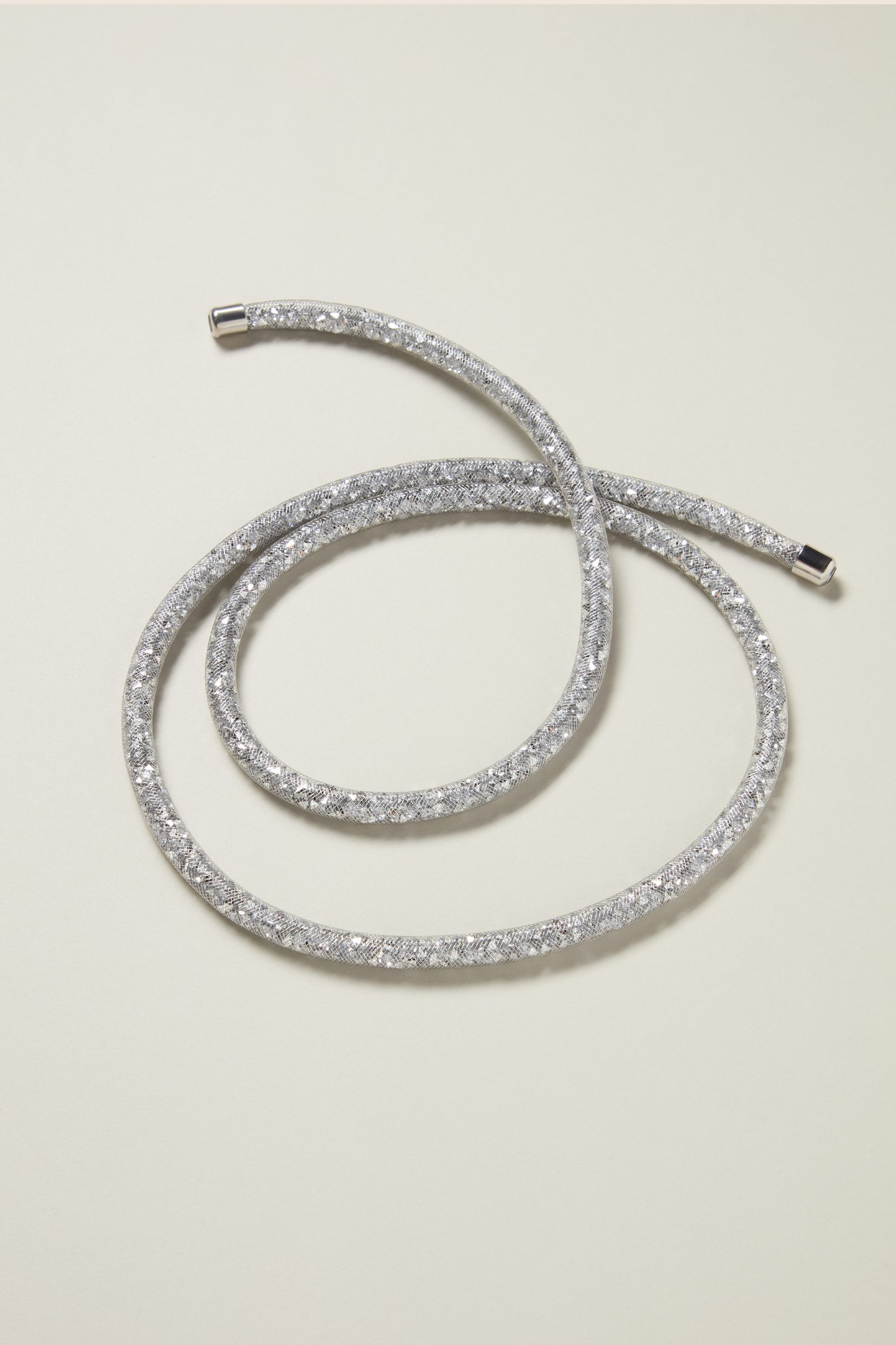 A flexible Long Diamante Necklace, featuring shimmering diamante stones, elegantly coiled in a circular pattern on a light-colored surface.