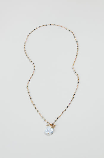 The Long Freshwater Pearl Necklace features delicate beads, a clear teardrop pendant, and a gold toggle clasp, beautifully displayed on a plain light background.