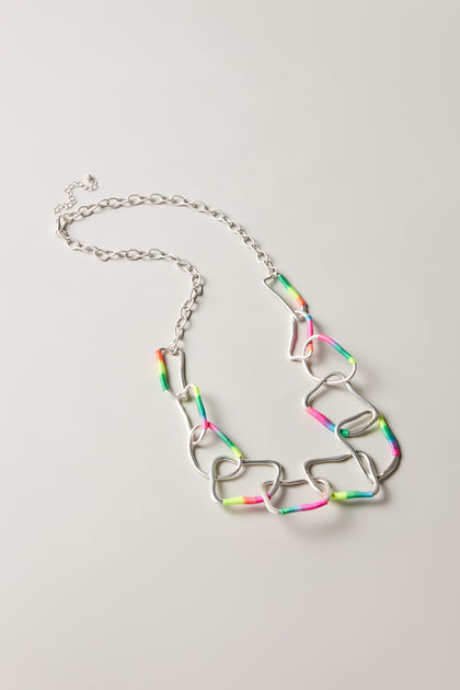 The Rainbow Detail Crushed Hoop Necklace features large, irregular silver links partially wrapped in neon pink, green, and yellow thread—perfect for colourful statement jewellery lovers—displayed on a light background.