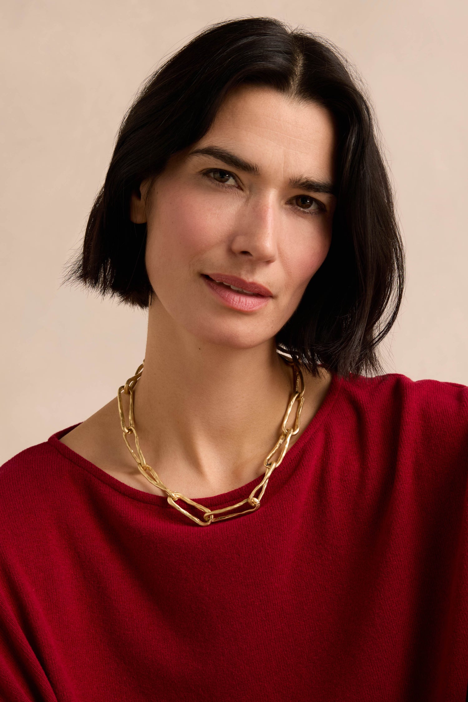 A woman with short dark hair wears the Short Gold Link Necklace and a red top, facing the camera against a neutral background.