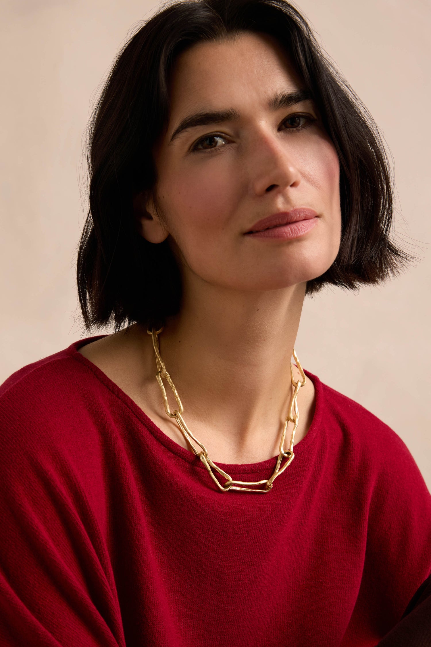 A woman with short dark hair wears a red top and the Short Gold Link Necklace, its textured surface adding an elegant touch as she looks at the camera with a neutral expression.