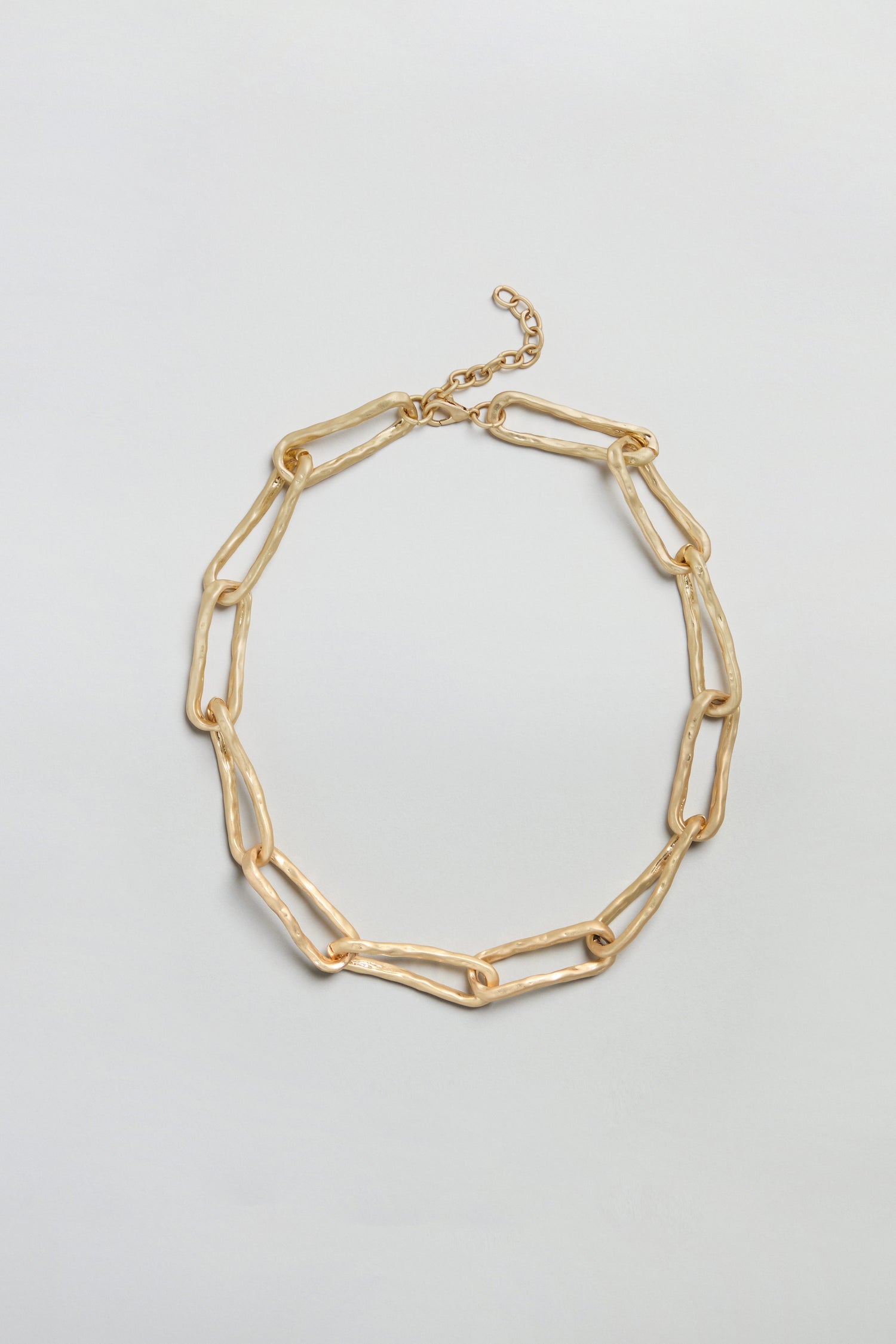 The Short Gold Link Necklace features large, irregular oval links with a textured surface and an adjustable clasp. This necklace is presented against a plain white background.