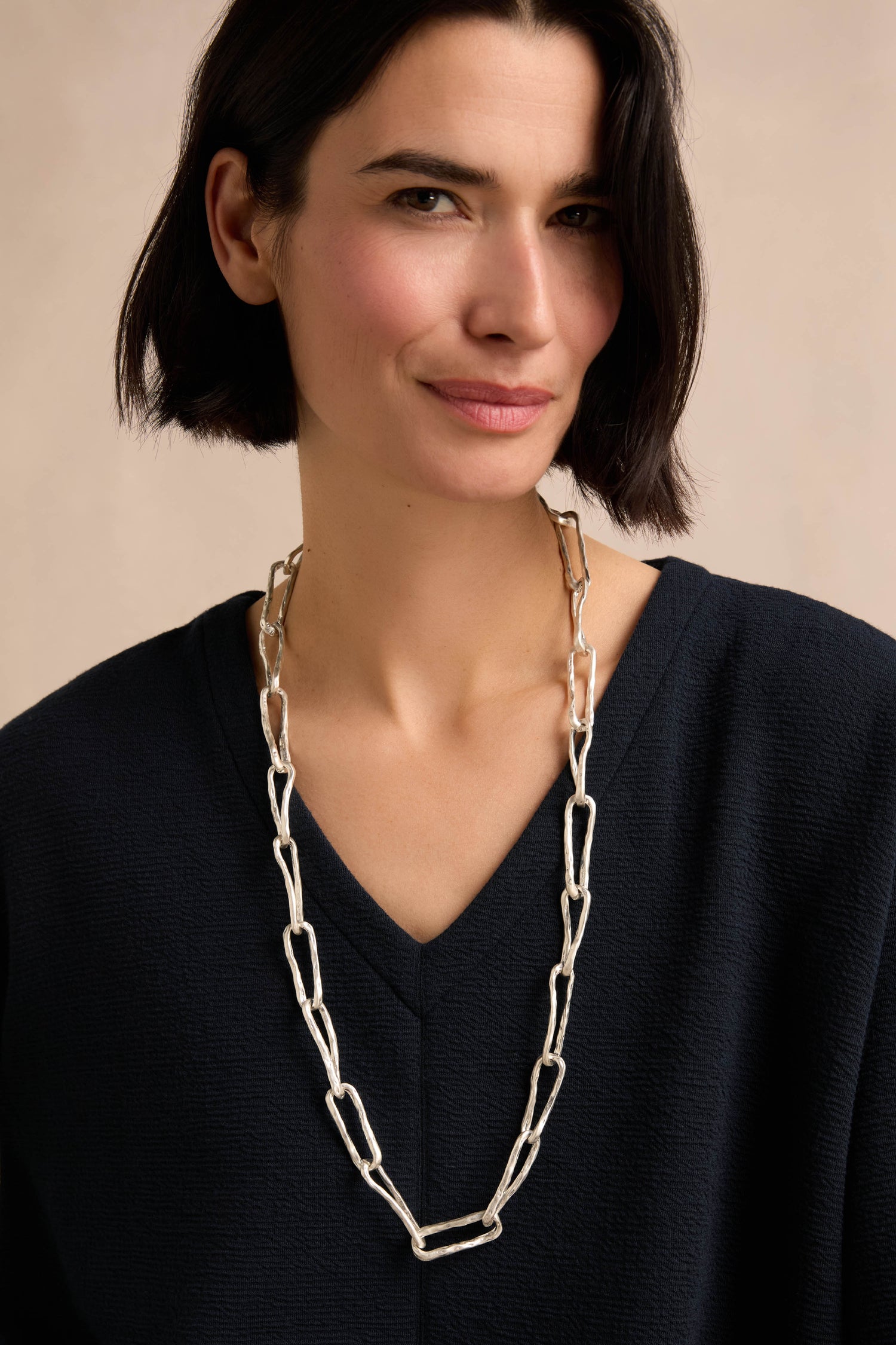 A person with short dark hair wearing a black top and the Long Silver Links Necklace stands against a neutral background.