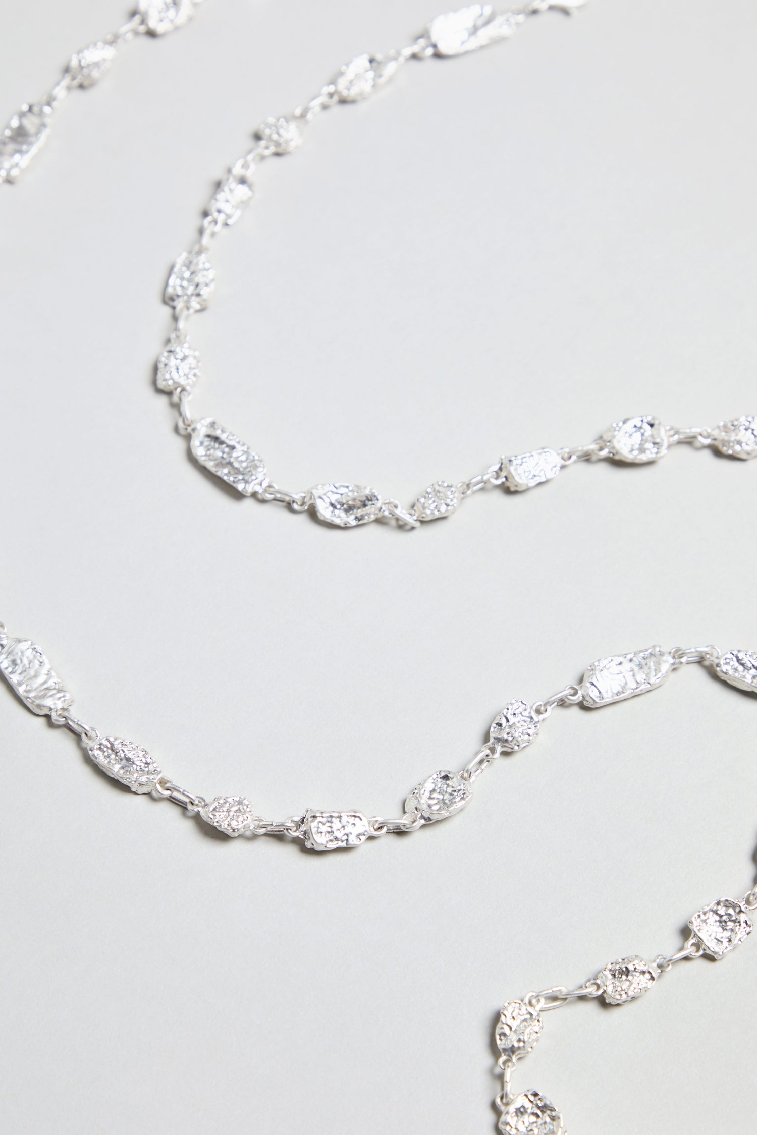 A detailed view of the Nugget Chain Necklace, featuring textured silver links with an irregular shape, displayed on a light background.