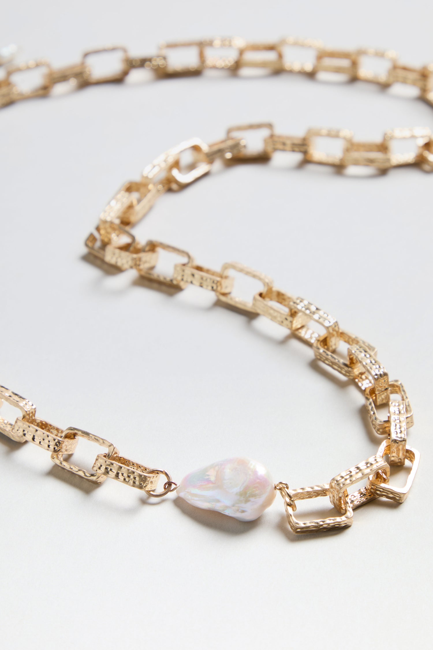 Gold Baroque Pearl Chain Necklace featuring rectangular textured gold links and a single irregular white pearl pendant, elegantly displayed on a neutral background—this necklace highlights the distinctive charm of baroque pearls in a sophisticated chain design.