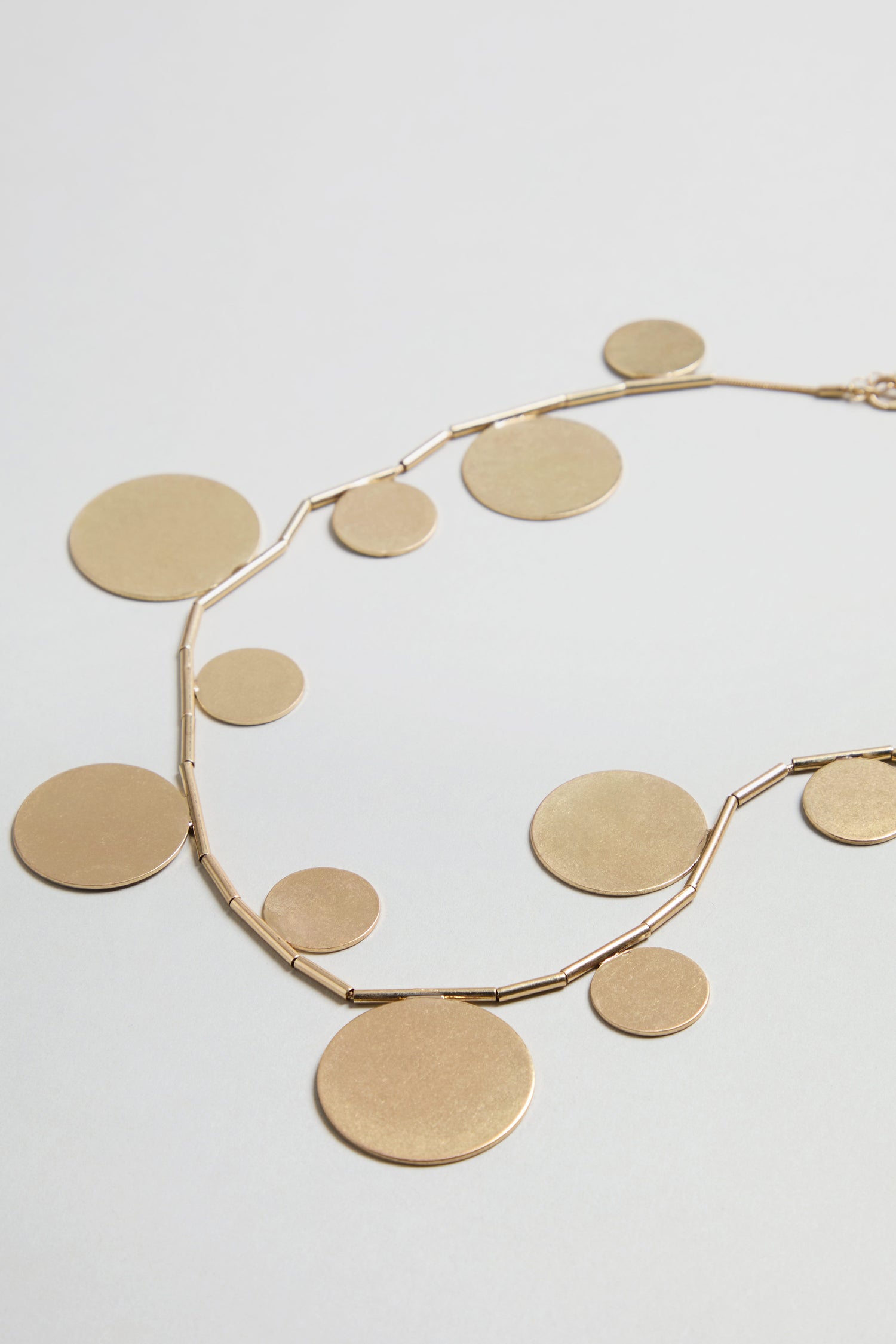 Orbit Disc Necklace featuring multiple flat, round gold discs in varying sizes displayed on a light surface.