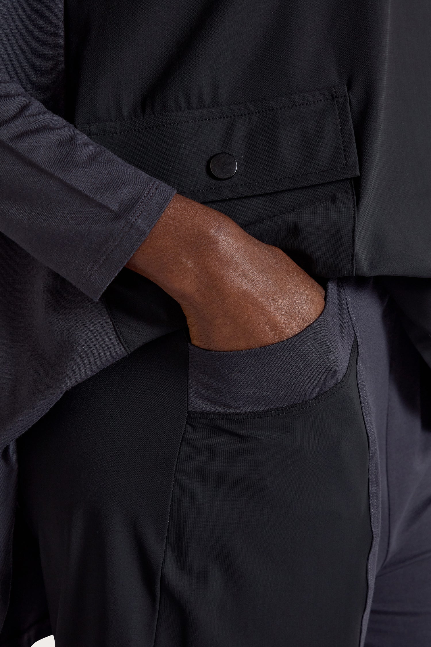 Close-up of a hand tucked into the pocket of a dark Panelled Jersey Trouser, highlighting the buttoned flap detail that showcases its minimalist design.