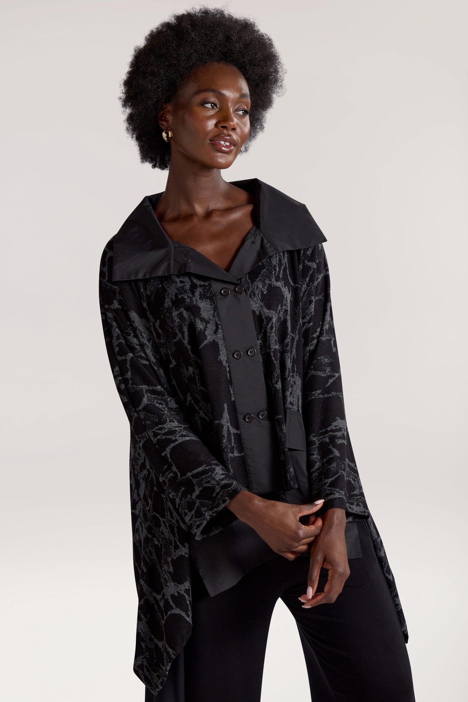 A person with an afro hairstyle is wearing the Big Pocket Wide Collar Jacket, featuring a black, buttoned design with an abstract digital print. They are standing and looking slightly to the side with a neutral expression on a plain background.