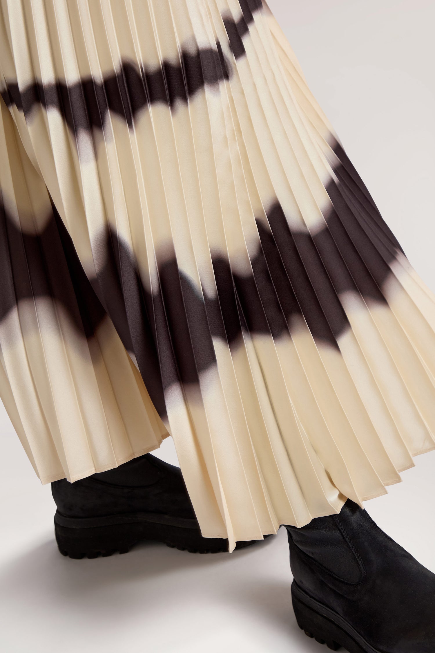 Close-up of a person wearing the Tie Dye Pleat Dress With Jersey Top, paired with black boots.