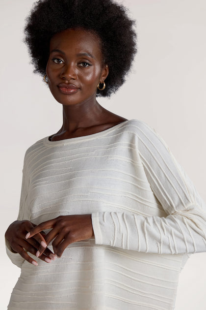 A person with a natural afro hairstyle, dressed in the Rib Detail Wide Neck Knit top in white, stands against a plain background, gazing at the camera.