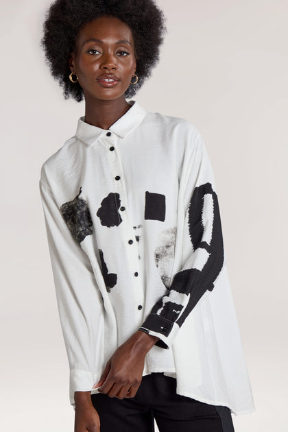 Person with an afro hairstyle wearing a white, long-sleeved Viscose Print Easy Shirt featuring black abstract patterns, standing against a light gray background.