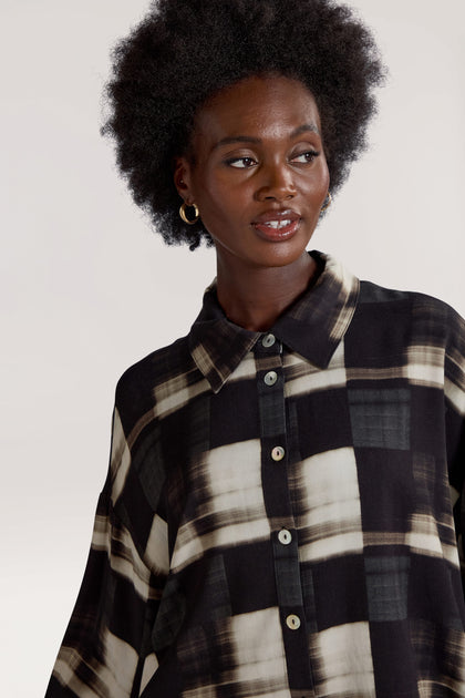 A person with an afro hairstyle wearing the Blurred Check Boxy Shirt in black and white stands against a neutral background, adding contemporary flair to the minimalist design.