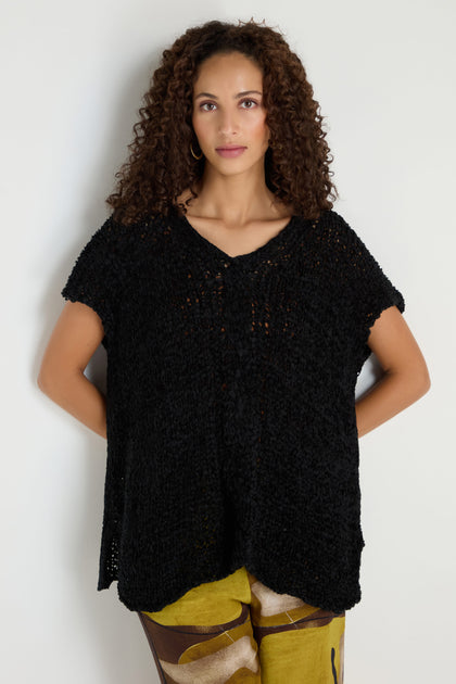 A woman with curly hair wears the V-Neck Cotton Blend Black Knit and yellow abstract-print pants, standing against a plain white background.