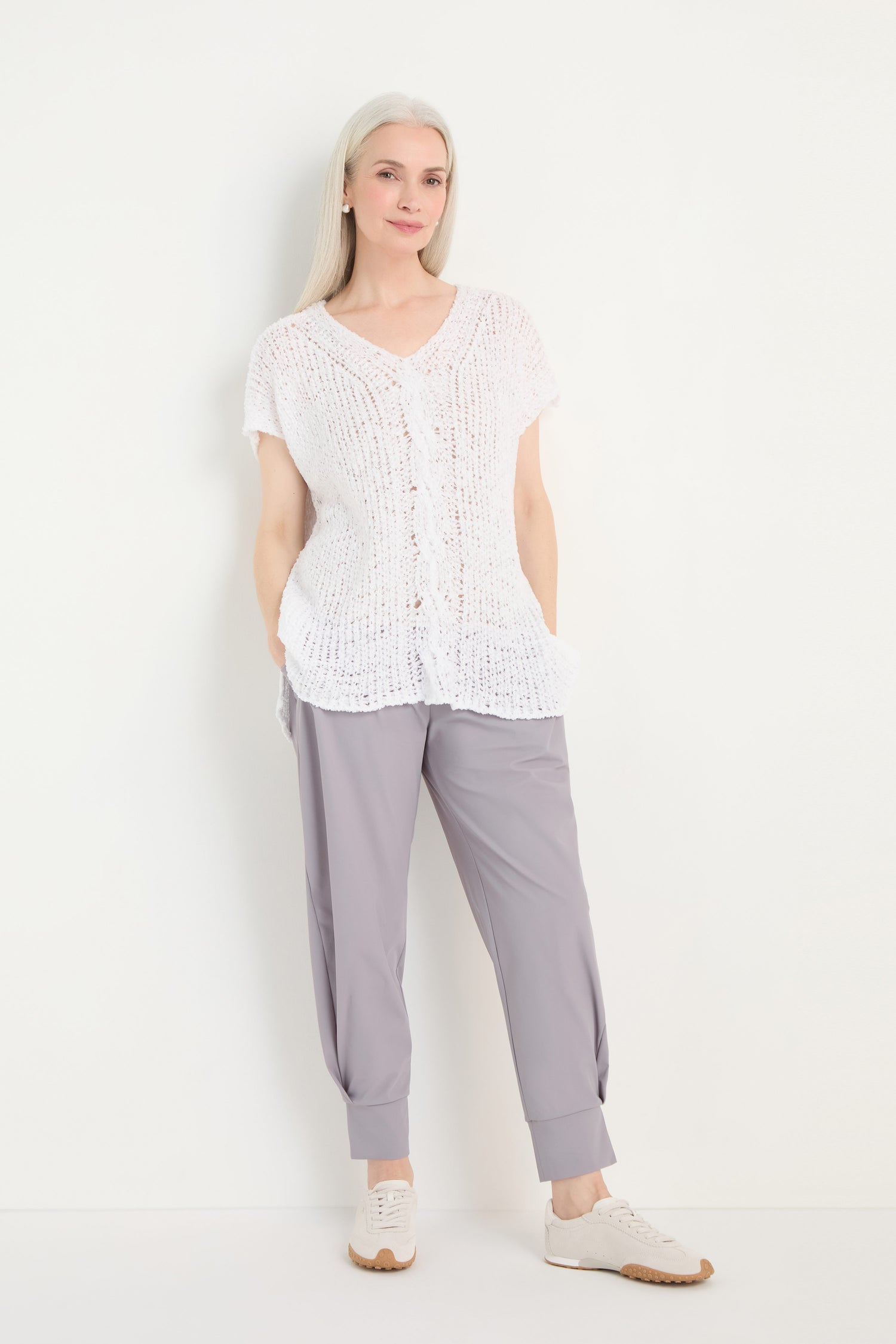 A woman with long light hair wears the V-Neck Cotton Blend Knit top, gray cuffed pants, and white sneakers, standing against a plain white background.