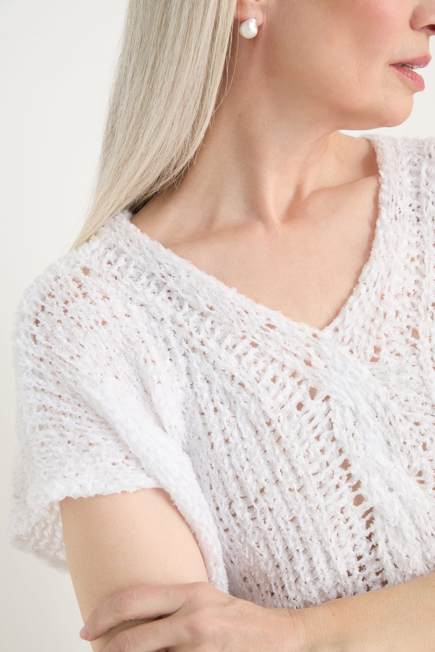 A close-up of a person with long, light hair wearing the V-Neck Cotton Blend Knit and pearl earrings, arms crossed.