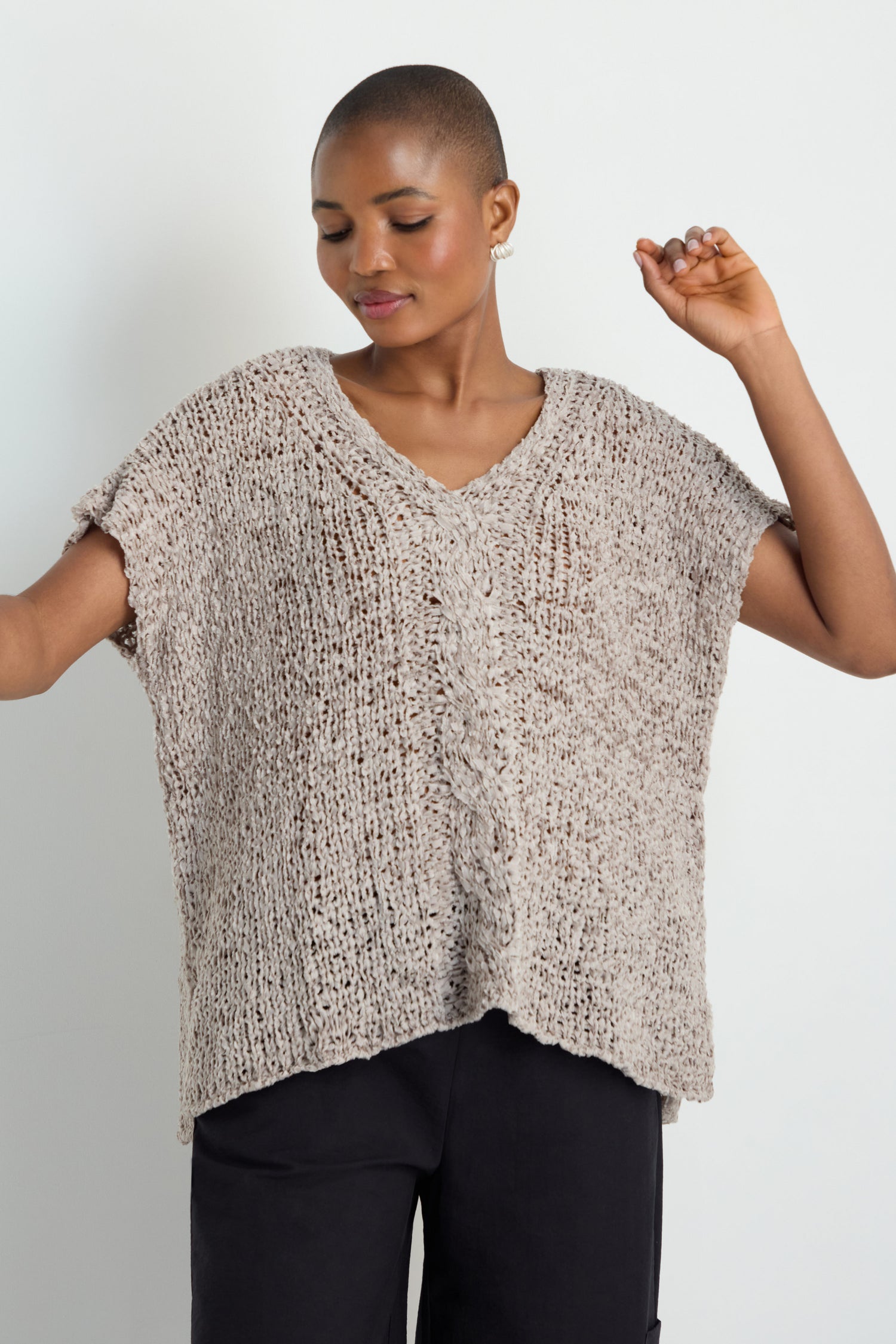 A person wears a loose, short-sleeved V-Neck Cotton Blend Knit in beige with black pants, standing against a plain light background.
