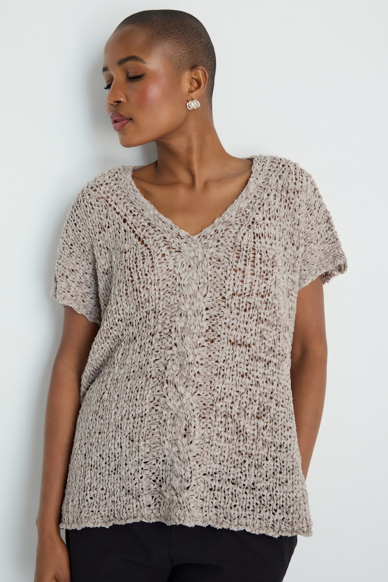 A woman with short hair wears the V-Neck Cotton Blend Knit, a textured beige short-sleeve top, paired with black pants against a plain white background.