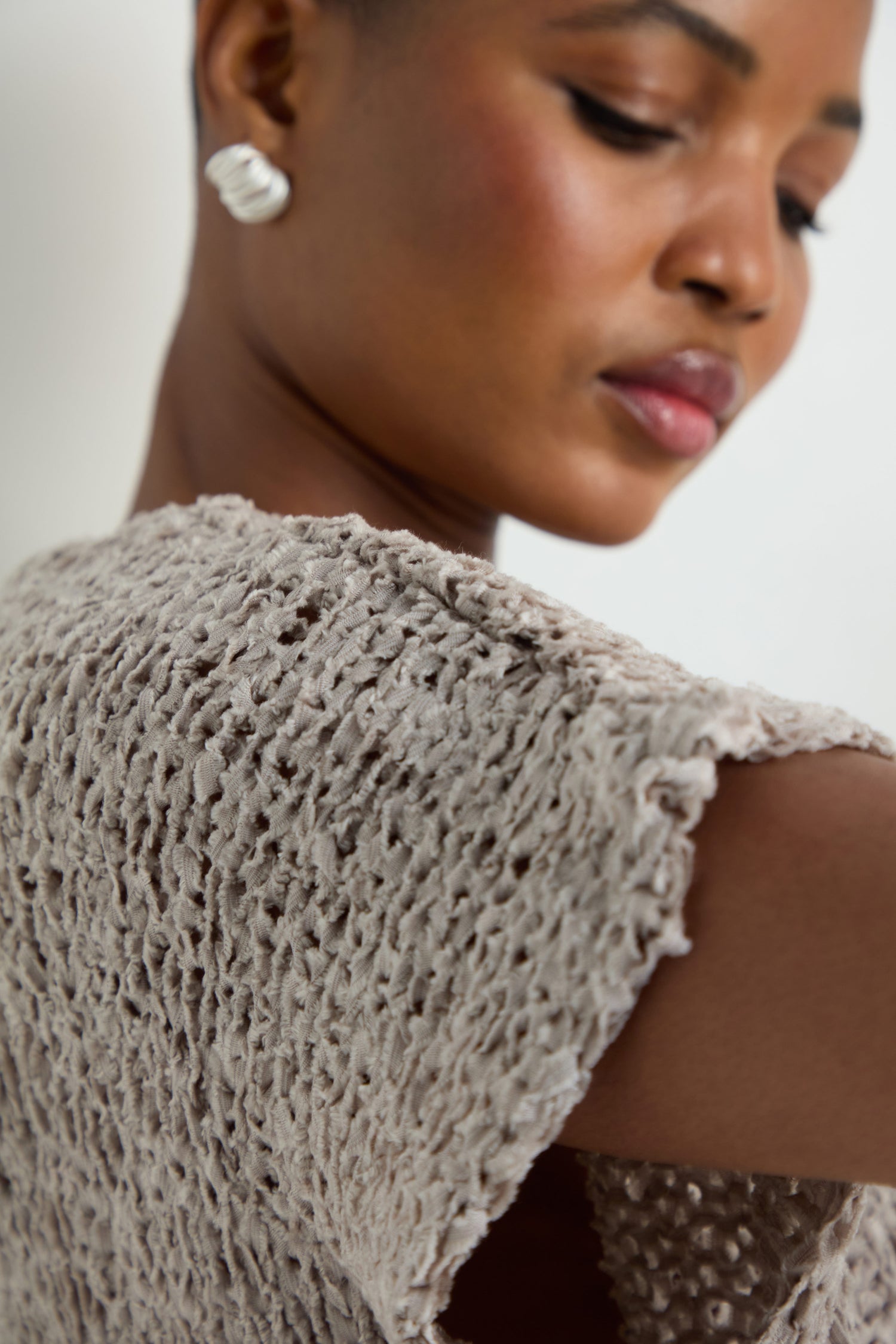 Close-up of a woman in the V-Neck Cotton Blend Knit, a light gray top with a textured open-weave, paired with a white earring and her face turned slightly to the side.