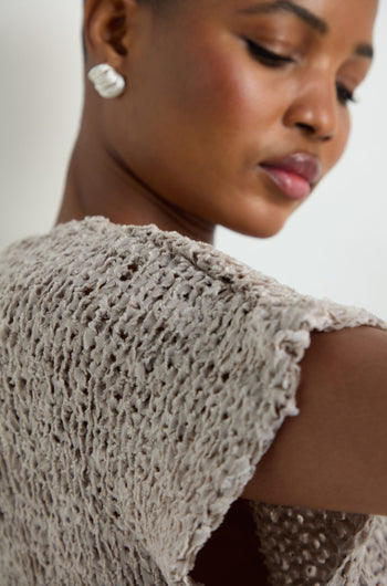 Close-up of a woman in the V-Neck Cotton Blend Knit, a light gray top with a textured open-weave, paired with a white earring and her face turned slightly to the side.