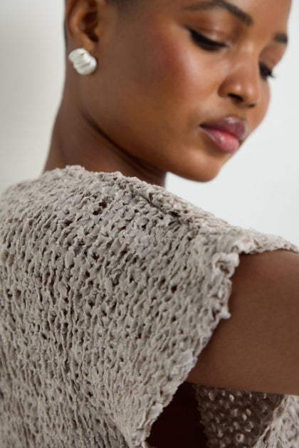 Close-up of a woman in the V-Neck Cotton Blend Knit, a light gray top with a textured open-weave, paired with a white earring and her face turned slightly to the side.