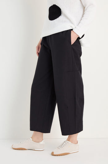 A person wearing a white sweater with a black circle, Wide Leg Cotton Trousers, and white sneakers stands with one hand in their pocket against a light background.